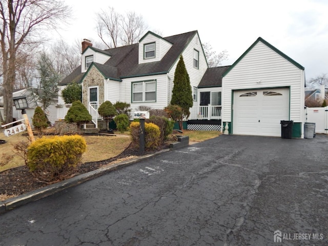 cape cod house with an attached garage, a chimney, fence, and aphalt driveway