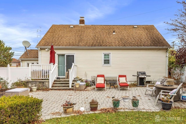 rear view of property featuring a shingled roof, a patio area, fence, and a chimney