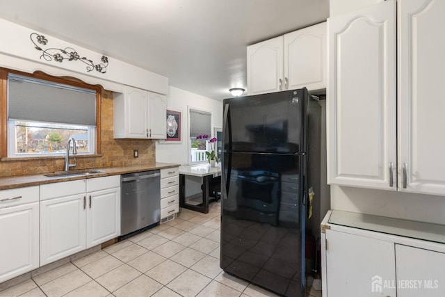 kitchen with light tile patterned floors, freestanding refrigerator, white cabinets, a sink, and dishwasher