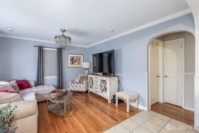 living room featuring arched walkways, baseboards, light wood-style flooring, and crown molding