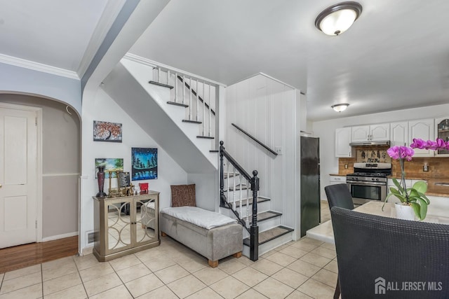 interior space with stairway, light tile patterned floors, arched walkways, and crown molding