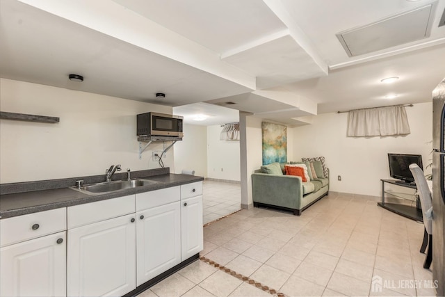 kitchen with dark countertops, stainless steel microwave, a sink, and white cabinetry