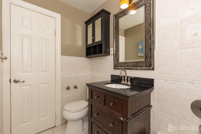 half bath featuring toilet, vanity, tile patterned flooring, and tile walls