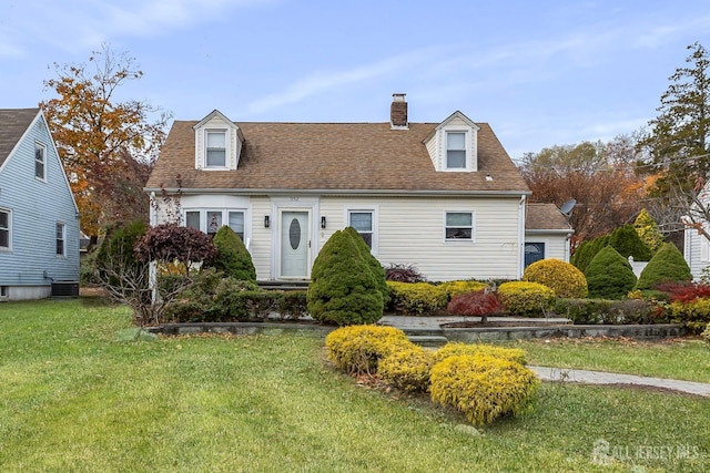 cape cod house with a shingled roof, a chimney, central AC unit, and a front yard