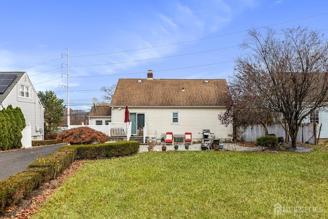 rear view of property with a shingled roof, a lawn, and a chimney