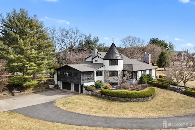 view of front of house featuring a front yard, a chimney, driveway, stone siding, and an attached garage