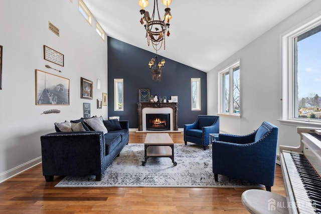 living area with baseboards, a lit fireplace, wood finished floors, a notable chandelier, and high vaulted ceiling