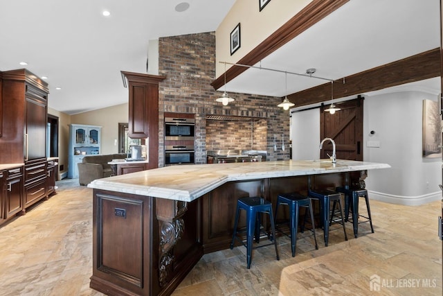 kitchen featuring double oven, a kitchen bar, a barn door, vaulted ceiling, and a large island