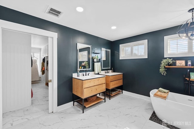 full bathroom featuring visible vents, two vanities, marble finish floor, baseboards, and a soaking tub