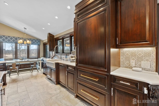 kitchen featuring tasteful backsplash, light countertops, lofted ceiling, hanging light fixtures, and a sink