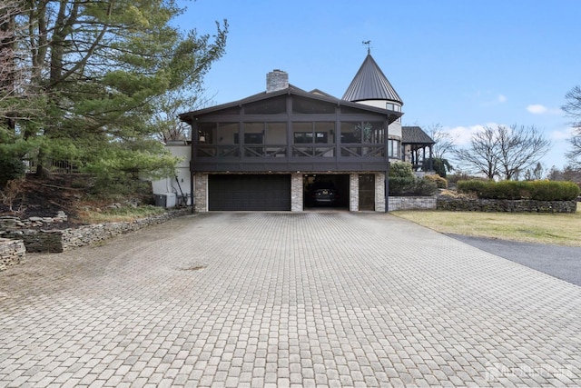 view of front of house with cooling unit, an attached garage, a sunroom, a chimney, and decorative driveway