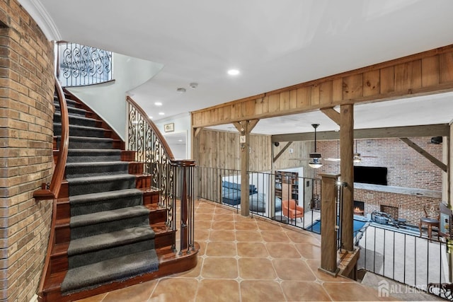 stairs with tile patterned floors, a warm lit fireplace, brick wall, crown molding, and wood walls