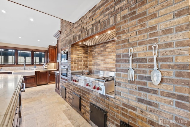 kitchen featuring brick wall, light countertops, stainless steel gas stovetop, custom exhaust hood, and a sink