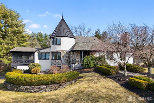 view of front of property with a front lawn, metal roof, a sunroom, stone siding, and a standing seam roof