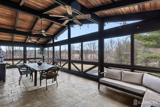 unfurnished sunroom with a view of trees, wood ceiling, ceiling fan, and vaulted ceiling with beams