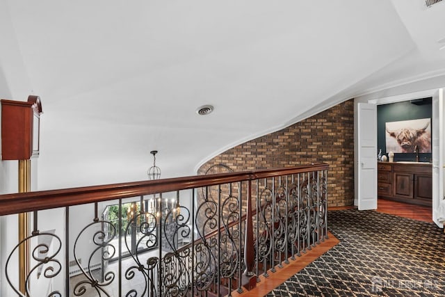 corridor with visible vents, brick wall, ornamental molding, vaulted ceiling, and a sink