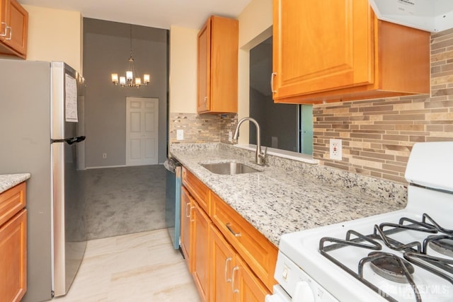 kitchen with light stone counters, a sink, appliances with stainless steel finishes, a notable chandelier, and backsplash