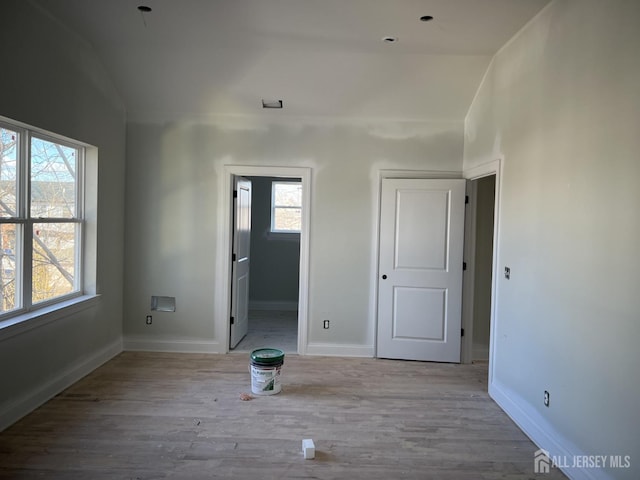 unfurnished bedroom featuring connected bathroom, multiple windows, vaulted ceiling, and light wood-type flooring