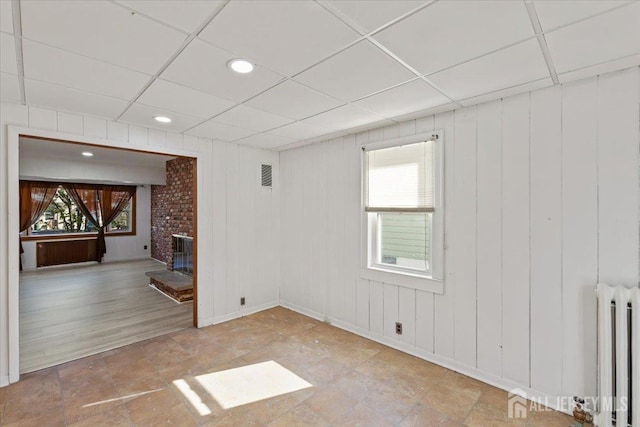 unfurnished room with a drop ceiling, plenty of natural light, visible vents, and radiator heating unit