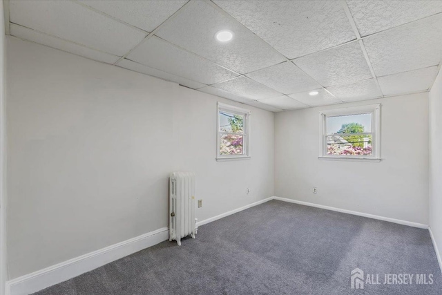 empty room with radiator heating unit, recessed lighting, a drop ceiling, baseboards, and dark carpet