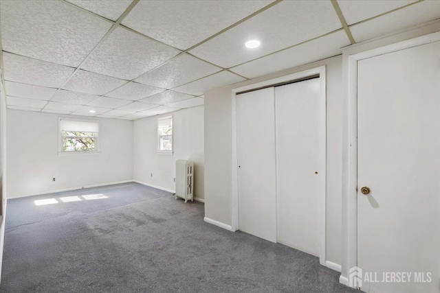 unfurnished bedroom featuring a drop ceiling, recessed lighting, baseboards, radiator, and carpet floors