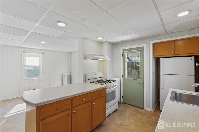 kitchen with a sink, radiator, white appliances, under cabinet range hood, and light countertops
