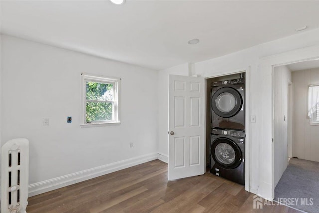 clothes washing area featuring radiator, wood finished floors, stacked washer / dryer, laundry area, and baseboards