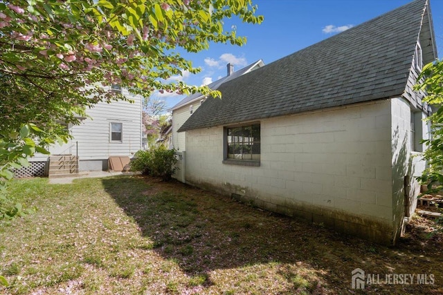 view of side of property with a shingled roof and concrete block siding