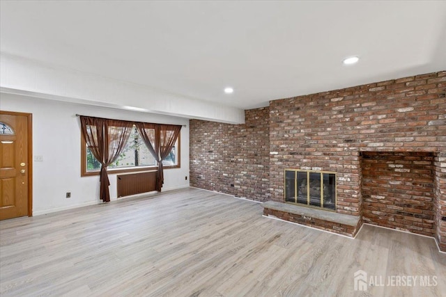 unfurnished living room with a fireplace, baseboards, brick wall, and wood finished floors