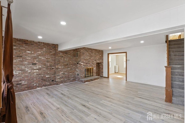unfurnished living room featuring wood finished floors, radiator, a fireplace, brick wall, and stairs