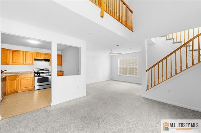 unfurnished living room with ceiling fan, light tile patterned flooring, light colored carpet, baseboards, and stairway