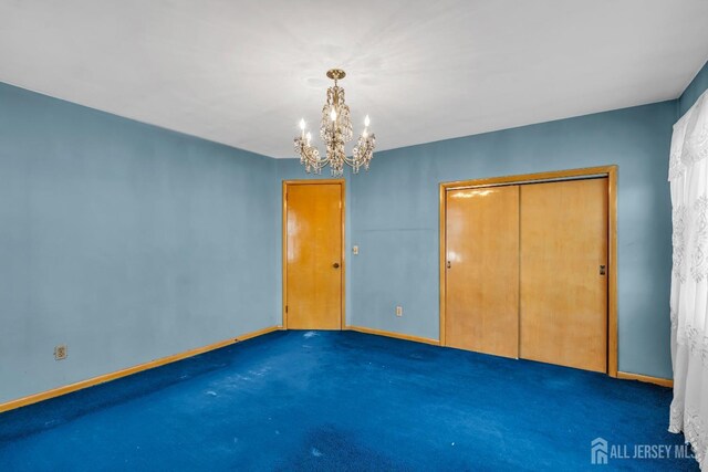 unfurnished bedroom with dark colored carpet, a chandelier, and a closet