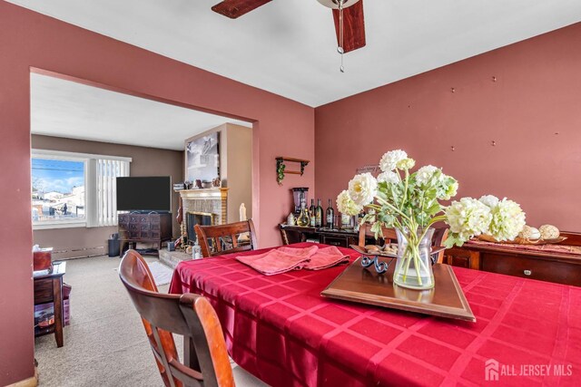 dining area featuring carpet flooring, a brick fireplace, ceiling fan, and a baseboard heating unit