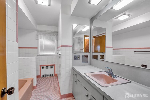 bathroom with vanity, radiator, tile patterned flooring, a tub to relax in, and tile walls