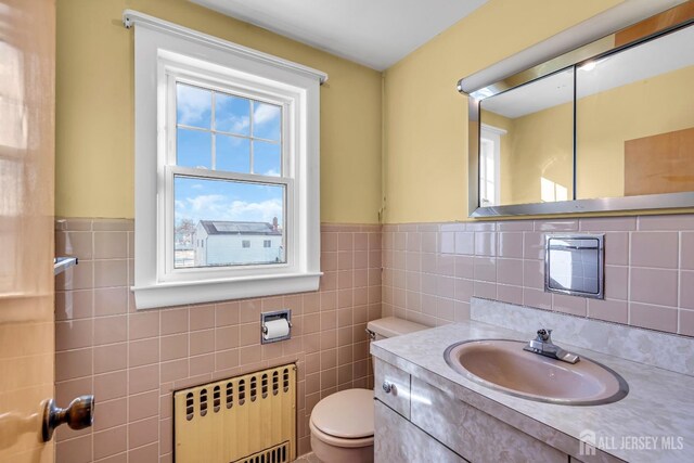 bathroom featuring radiator heating unit, vanity, tile walls, and toilet