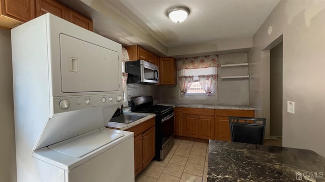 kitchen featuring stacked washer / drying machine, black range with electric stovetop, sink, and light tile patterned floors