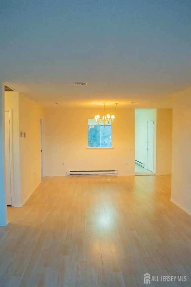 empty room with hardwood / wood-style floors, a chandelier, and a baseboard heating unit