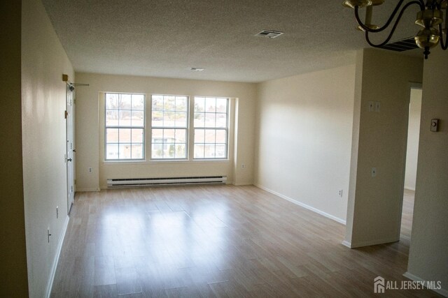 unfurnished room featuring baseboard heating, light wood-type flooring, a textured ceiling, and a chandelier