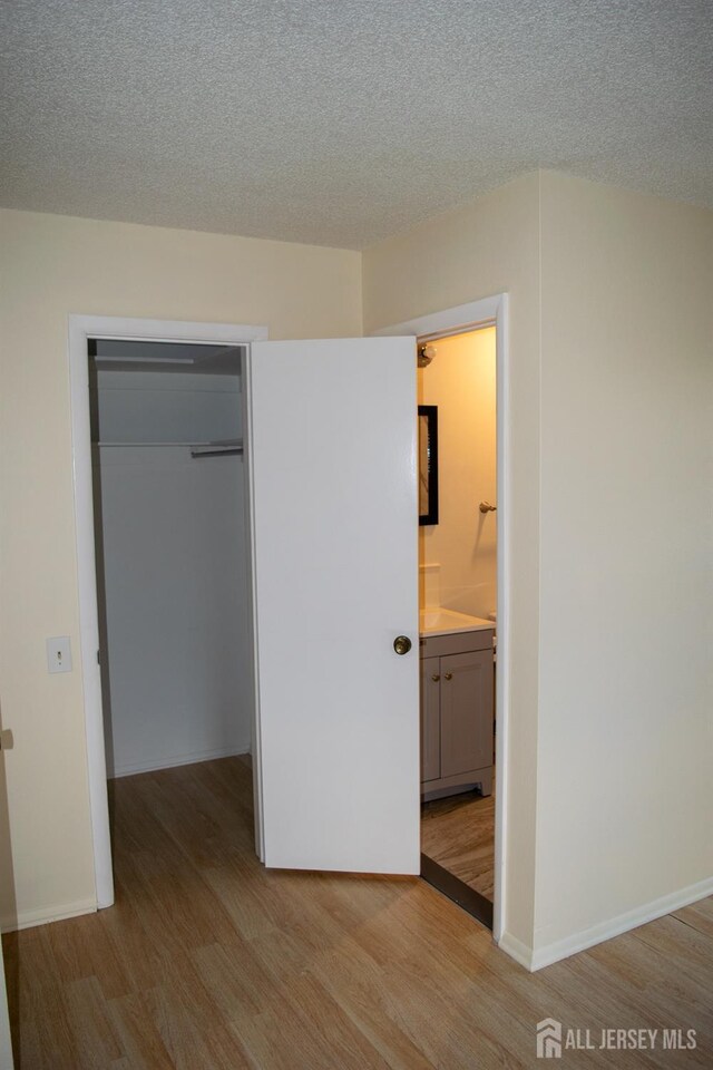 unfurnished bedroom with ensuite bath, light wood-type flooring, a closet, and a spacious closet