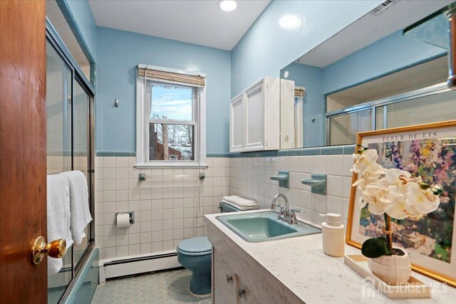 full bath featuring toilet, a wainscoted wall, a shower with shower door, and a baseboard radiator