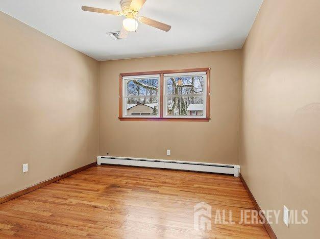 spare room featuring baseboard heating, a ceiling fan, baseboards, light wood-type flooring, and visible vents