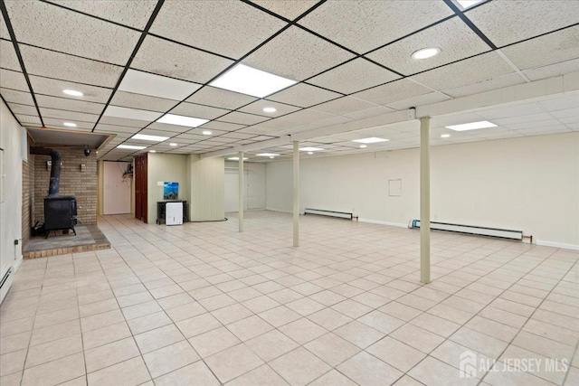basement with a baseboard radiator, a wood stove, and a drop ceiling