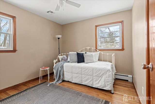 bedroom featuring a ceiling fan, visible vents, wood finished floors, baseboards, and a baseboard radiator