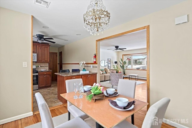 dining space featuring baseboards, ceiling fan with notable chandelier, light wood finished floors, and visible vents