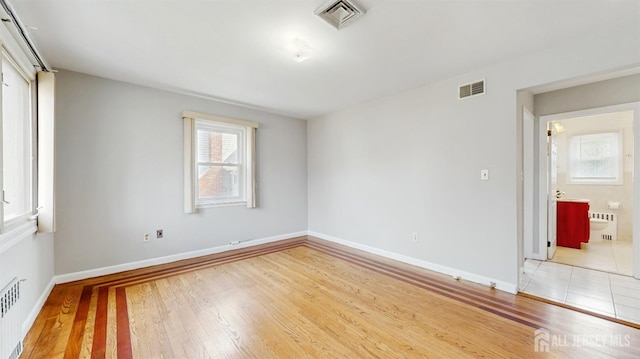 spare room featuring baseboards, visible vents, wood finished floors, and radiator