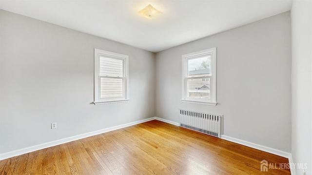 spare room with baseboards, radiator heating unit, and light wood-style flooring