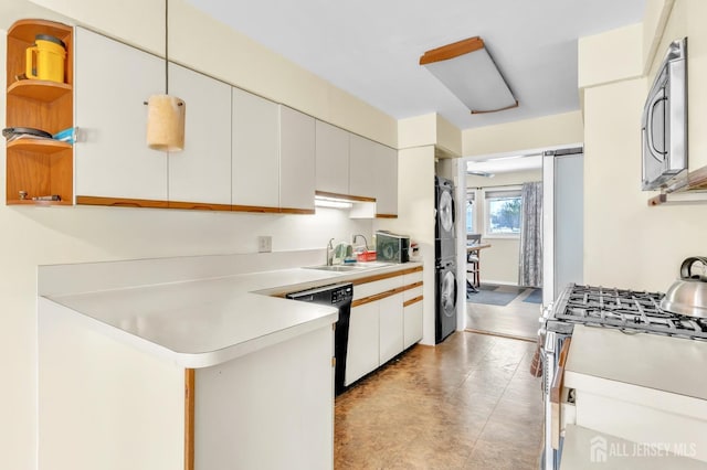 kitchen with stacked washer and dryer, a peninsula, stainless steel appliances, light countertops, and a sink