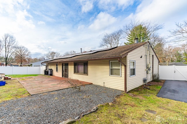 rear view of house featuring a fenced backyard, a gate, a deck, and roof mounted solar panels