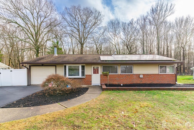 ranch-style home featuring an attached garage, brick siding, fence, roof mounted solar panels, and a front yard