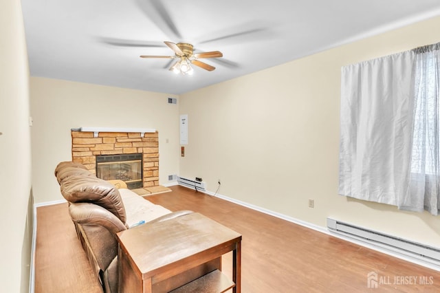 living room with a baseboard heating unit, ceiling fan, a stone fireplace, and baseboards